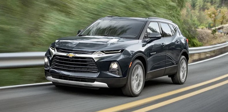 Brand new black 2022 Chevrolet Blazer driving down a foresty highway road.