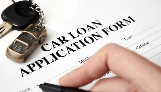 A close of picture of a person filing out a car loan application with a car key right above the form title.