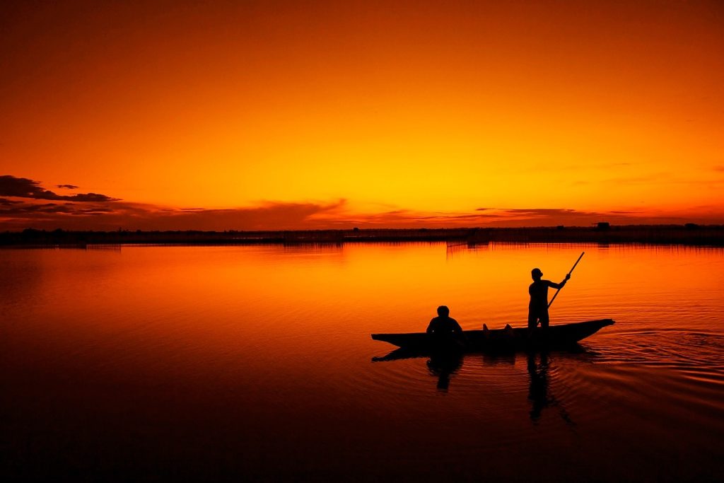 two people on a boat fishing at sunset