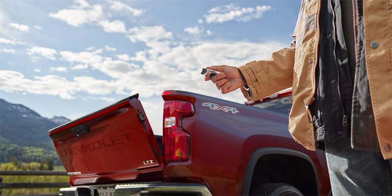 Image showcasing a man using the key fob to his new 2023 Chevrolet Silverado 3500 to put down the tail gate without any manual labor.