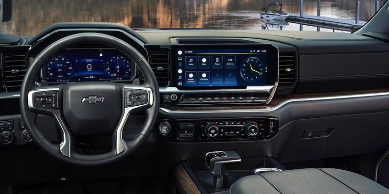 The image features the interior of a car, specifically the dashboard of a 2024 Chevrolet Silverado 1500. The dashboard is equipped with a large touch screen display, which is likely used for navigation and other vehicle functions. The car's steering wheel is also visible in the image, providing a clear view of the dashboard and the screen.